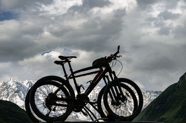 Fototapeta na wymiar silhouettes of two bicycles on a background of snowy mountains in the Caucasus