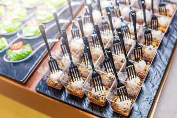 Delicious salad served in mini glasses with forks on a black tray. Fancy food snacks on a event party or wedding