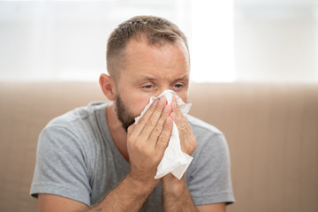 Sick man blowing nose and sneeze into tissue. Male have flu, virus or allergy respiratory. Healthy, medicine and people concept.  Headache and fever remedies.