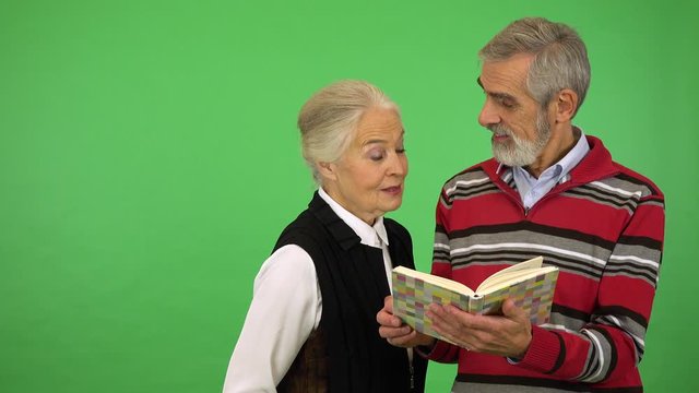 A smiling elderly couple reads from a book - green screen studio