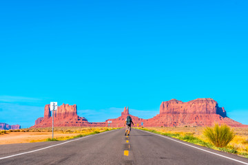 Fototapeta na wymiar A young man with white t-shirt and green backpack on the road of Monument Valley. Utah
