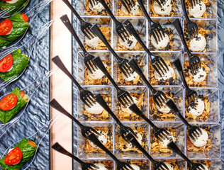 Fancy food snacks on a banquet table. Delicious salad served in mini glasses with forks on a black tray. Top view