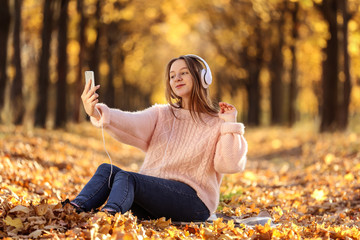 Young beautiful girl with headphones making selfie in autumn park