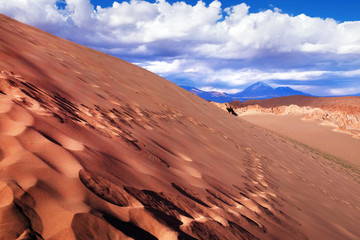 Fototapeta na wymiar View of sand dunes and rocky hills in the Mars Valley near San Pedro de Atacama against a blue dramatic sky above volcanoes.