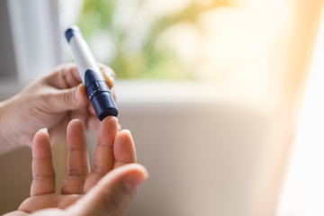 Close up of woman hands using lancet on finger to check blood sugar level by Glucose meter in the morning. Use as Medicine, diabetes, glycemia, health care and people concept.