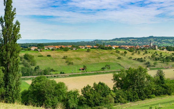 Hilly and picturesque landscape view of meadows, pastures, fields, trees, town of Brens and white clouds in the blue sky.Department of Haute-Savoie,region of Auvergne-Rhone-Alpes in France.