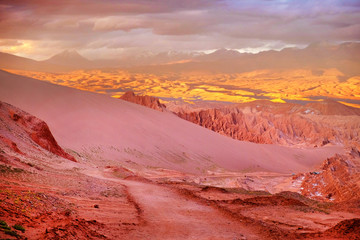 Fototapeta premium Panoramic view of the Mars Valley near San Pedro de Atacama against a warm and colorful sunset sky above volcanoes.