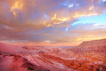 Panoramic view of the Mars Valley near San Pedro de Atacama against a warm and colorful sunset sky above volcanoes.