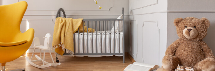 Panoramic view of cute yellow and grey baby bedroom with teddy bear, rocking horse, egg chair and...