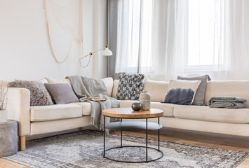 Beige comfortable corner sofa with grey pillows in elegant living room interior with white wall