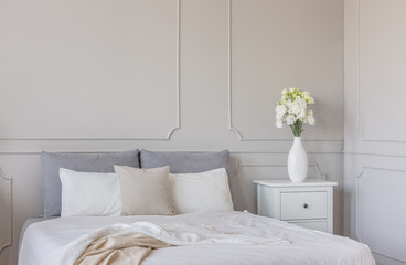 Flowers on white wooden nightstand table in luxury bedroom interior with king size bed