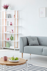 Pears on plate on wooden coffee table in trendy living room interior with comfortable grey couch and white shelf, real photo