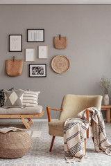 Trendy creme colored armchair in Scandinavian living room interior with gallery of posters on beige wall