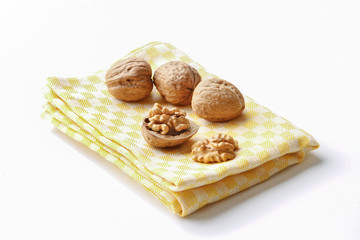 group of cracked walnuts on a kitchen cloth on a white backdrop