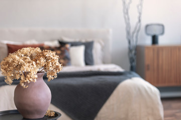 Brown flowers in pottery vase on metal nightstand next to king size bed in scandinavian bedroom interior