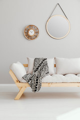 Round mirror and wooden clock on the empty wall of spacious living room interior with beige...