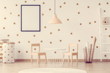 Pastel pink lamp above small trendy white table with wooden chairs in scandinavian kid's room
