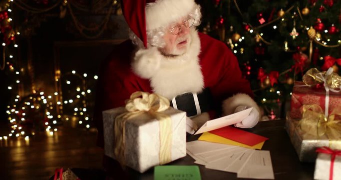 Santa Claus  is sitting at the table, reading letters and chooses gifts for children in a room decorated for Christmas. Christmas and New Year time. 