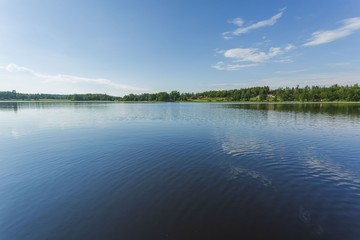 Beautiful view on lake on summer day. Dark blue lake water surface, green tall trees and blue sky with white clouds. Sweden, Europe.	