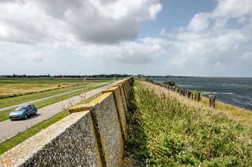 View along the dike on the north coast of the island of Schouwen-Duiveland, The Netherlands, with a weathered concrete wall, Lake Grevelingen on one side and a road and meadows on the other side