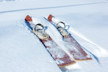 Pair of old fashioned wooden brown skis on white snow. Vintage winter background.