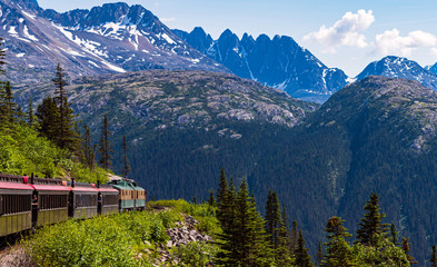 a narrow guage tour train hugs the cliff on the white pass gorge through the mountains near skagway...