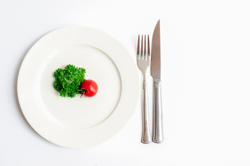 Close up top view of green parsley and red tomato on white dish with knife and fork with copy space on white background, Diet food, vegan and  vegetarian food concept.