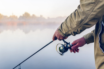Hands of a fisherman with a spinning rod and coil summer morning on the lake