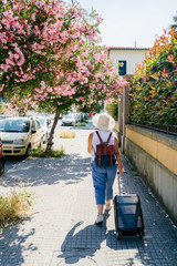 Woman in hat with suitcase and backpack is walking on city street in sunny summer day. Italy, Europe