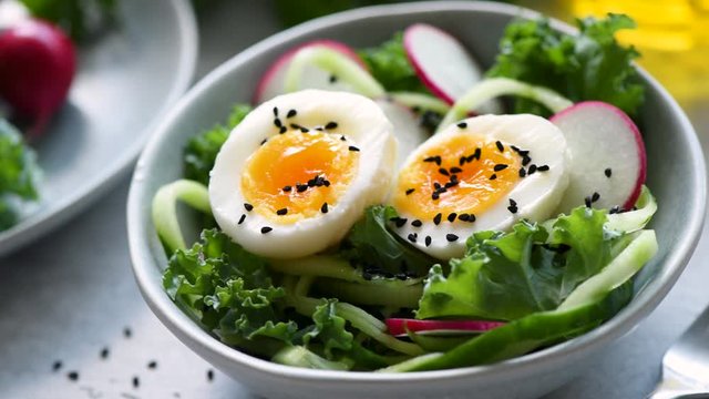 Egg cucumber salad with kale and radish. Healthy vegetarian green salad rotating in a bowl, closeup view. Concept of clean eating, dieting