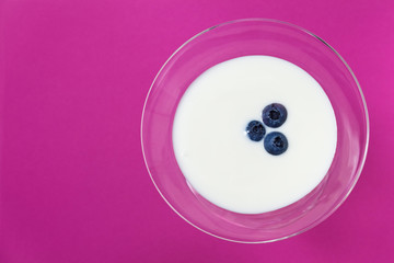 Fresh yoghurt with blueberries in a glass on pink background.