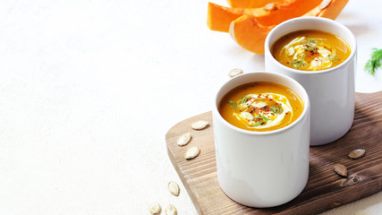 Roasted pumpkin and carrot soup with cream and pumpkin seeds on two white mug on white background with black bread slices.Vegetarian eating.Diet and healthy food concept.Space for copy and text