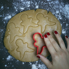 Female hands in flour making Christmas cookie in the form of gingerbread man from dough in kitchen. Home baking process