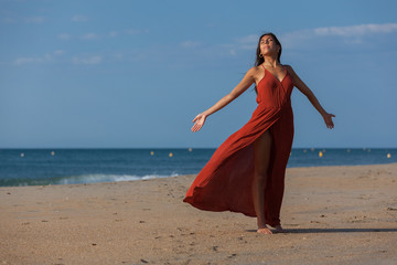 Pretty young woman in a red dress and nude foots on the sand of the beach. Happy girl enjoying freedom at the sea..