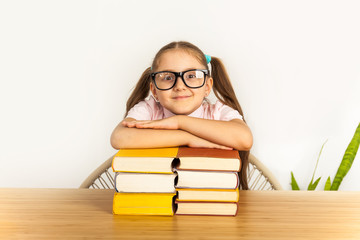 Smiling little student girl with many books at school