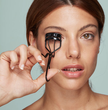 Woman curling eyelashes in colourful isolated setup