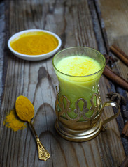 Golden milk with turmeric powder in glasses over wooden background, copy space. Health and energy boosting, flu remedy, natural cold fighting drink. Clean eating, detox, weight loss concept