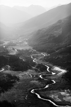 A black and white image of a river snaking through a valley in the mountains