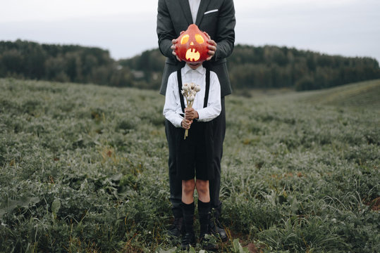 Man and boy standing in field with Halloween pumpkin