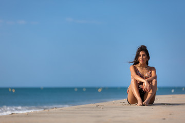 Fototapeta na wymiar Calm young woman sitting alone on a sand beach. Relaxing and harmony concept..