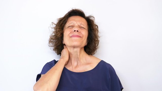 Mature caucasian woman holding her neck behind as she having headache and feeling pain in the neck and back. Shot in 4K, white background