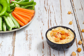 Hummus platter with assorted snacks. Hummus in bowl, vegetables sticks, chickpeas, olives. Plate with Middle Eastern/Mediterranean meze. Party/finger food. Top view. Vegetables, hummus dip,copy space