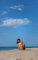 Happy young woman sitting alone on a sand beach. Relaxing and  harmony concept..