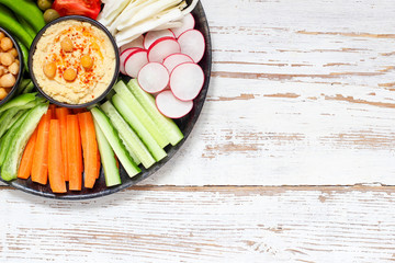 Hummus platter with assorted snacks. Hummus in bowl, vegetables sticks, chickpeas, olives. Plate with Middle Eastern/Mediterranean meze. Party/finger food. Top view. Vegetables, hummus dip,copy space