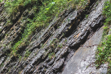 Multilayered dark rocky geological layers on the bank of a mountain river. Rock with visible geological layers_