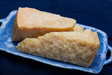 Italian original aged Parmesan cheese in two pieces served on blue plate close up