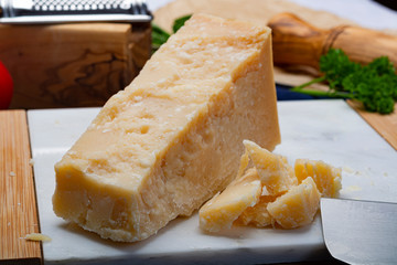 One piece of Italian original aged Parmesan cheese on white marble board close up