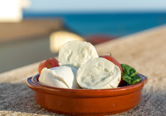 Italian mozzarella soft cheese in balls served with tomatoes and fresh basil outdoor with blue sea view
