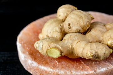 Fresh ginger roots on pink salt board close up on black wooden background