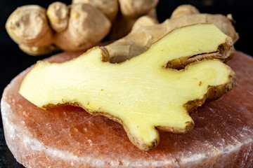 Fresh ginger roots on pink salt board close up on black wooden background
